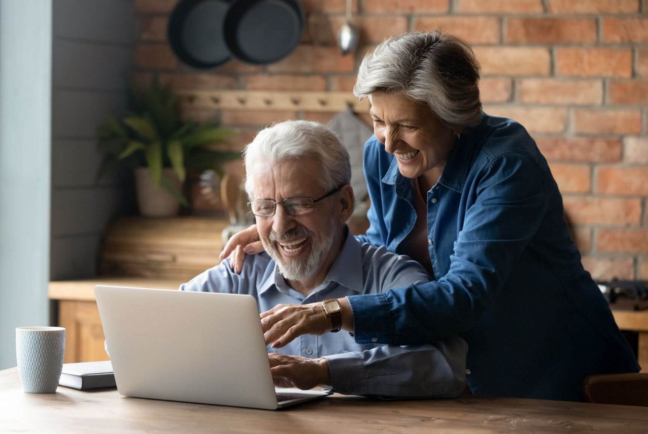 Ein lächelndes Ehepaar bedient einen Laptop und erstellt die Betriebskostenabrechnung.