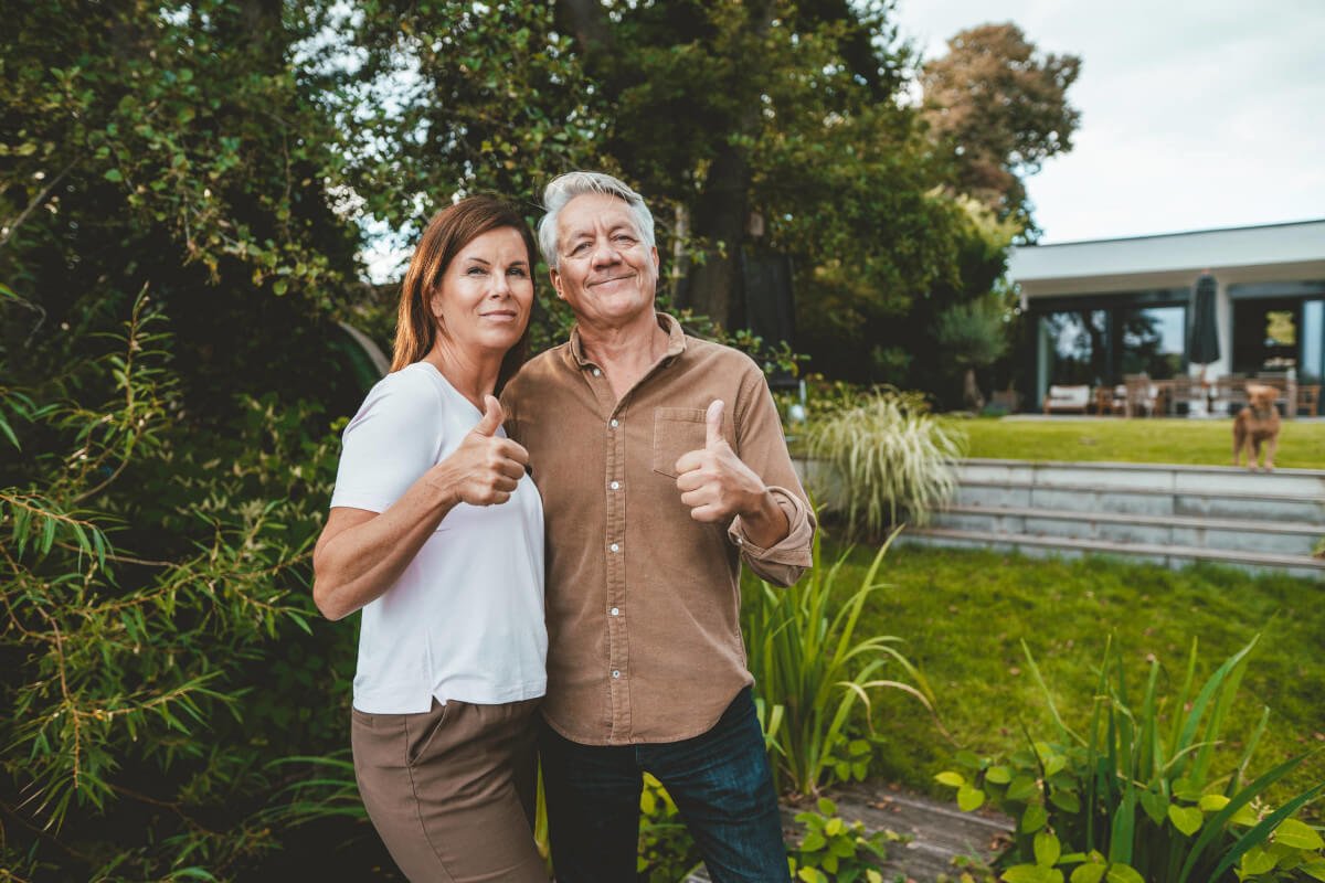 Mann und Frau stehen vor einem Baum und halten ihren Daumen hoch
