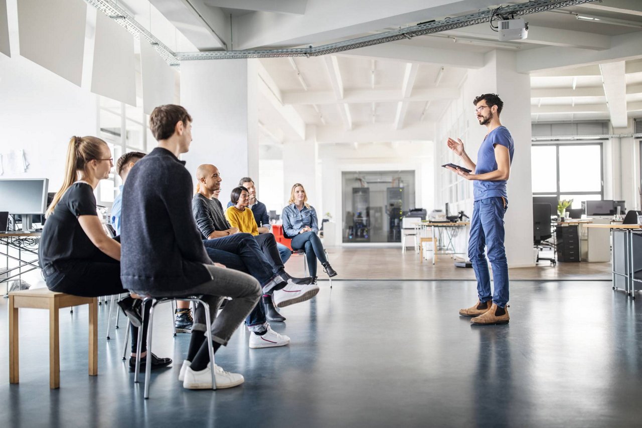 Young man discussing new ideas with team at a meeting. Businessman speaking in front of small audience at office meeting.