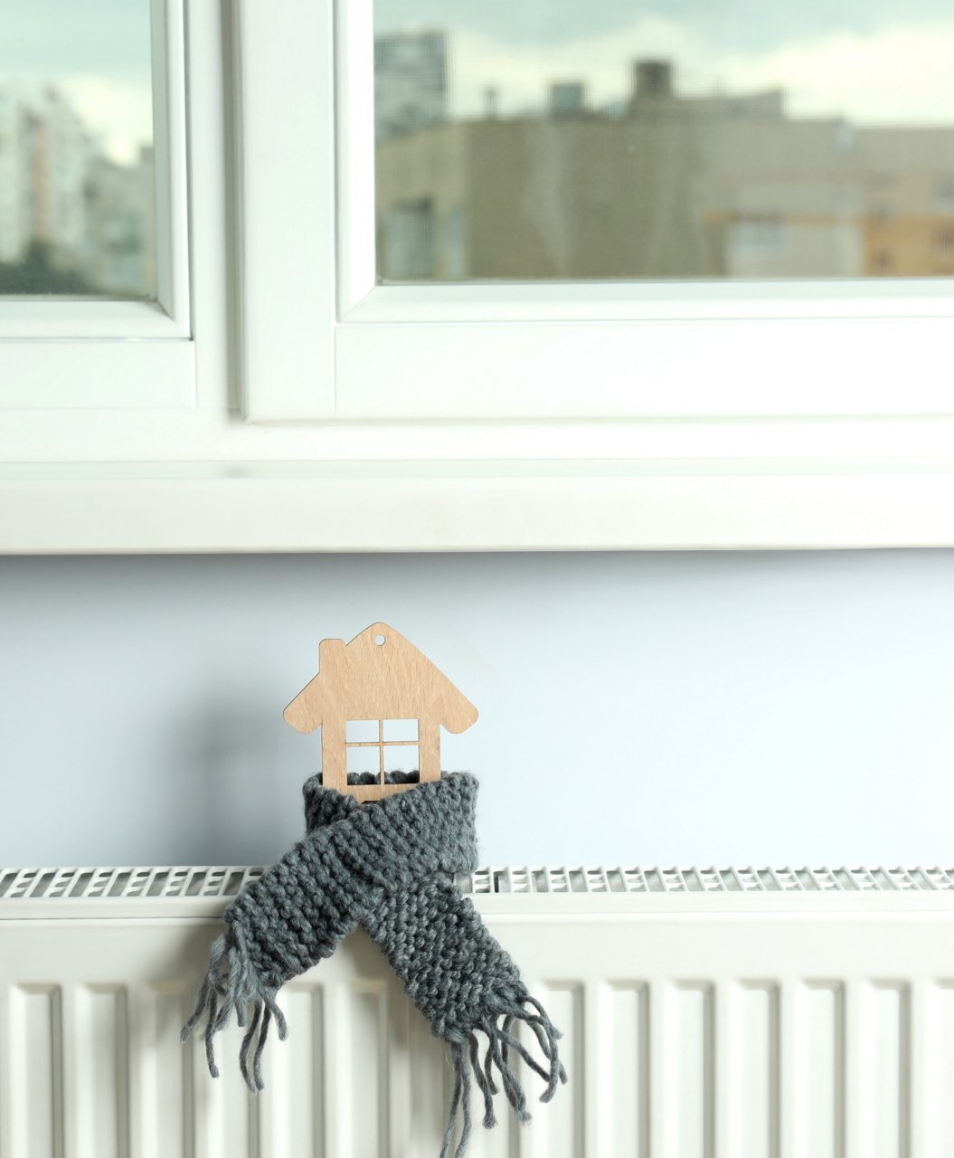 Termosifone all'interno di un'abitazione con un inserto di legno a forma di casa e la sciarpa di lana per parlare di ripartizione delle spese del calore all'interno del condominio con Techem