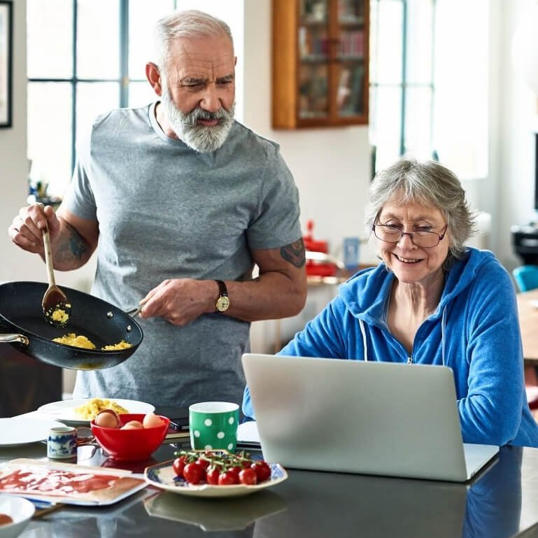 Mann in der Küche am Kochen und Frau sitzt vor dem Laptop