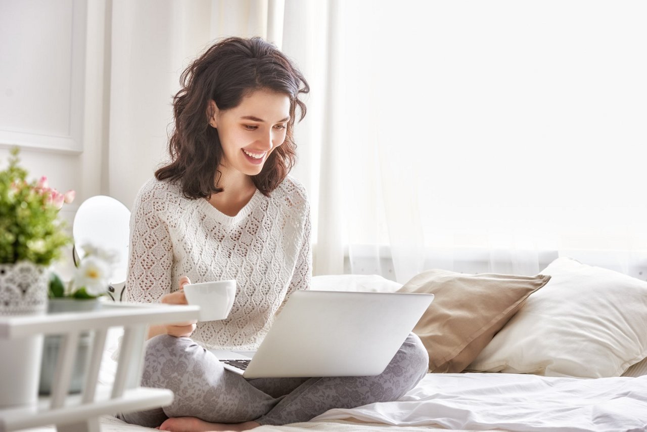 Frau mit Laptop und Tasse auf Bett