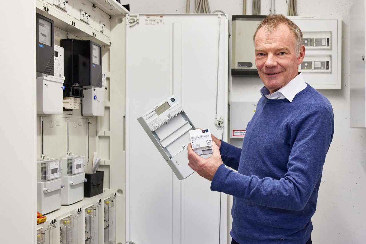 Gero Lücking holds a digital electricity meter in his right hand. This, in conjunction with the smart meter gateway (in his left hand), creates an intelligent metering system.