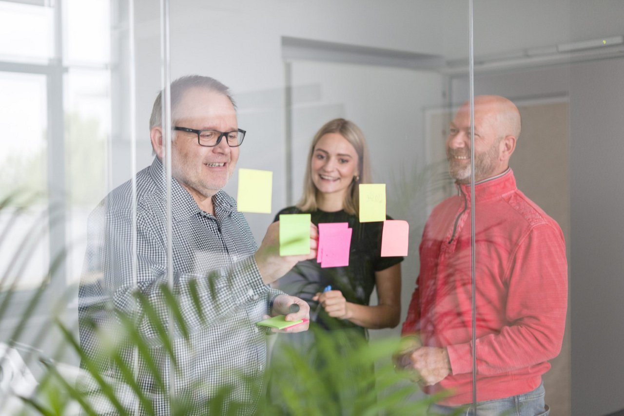 Flere personer i et møterom som henger opp post-it lapper i forskjellig farger. 