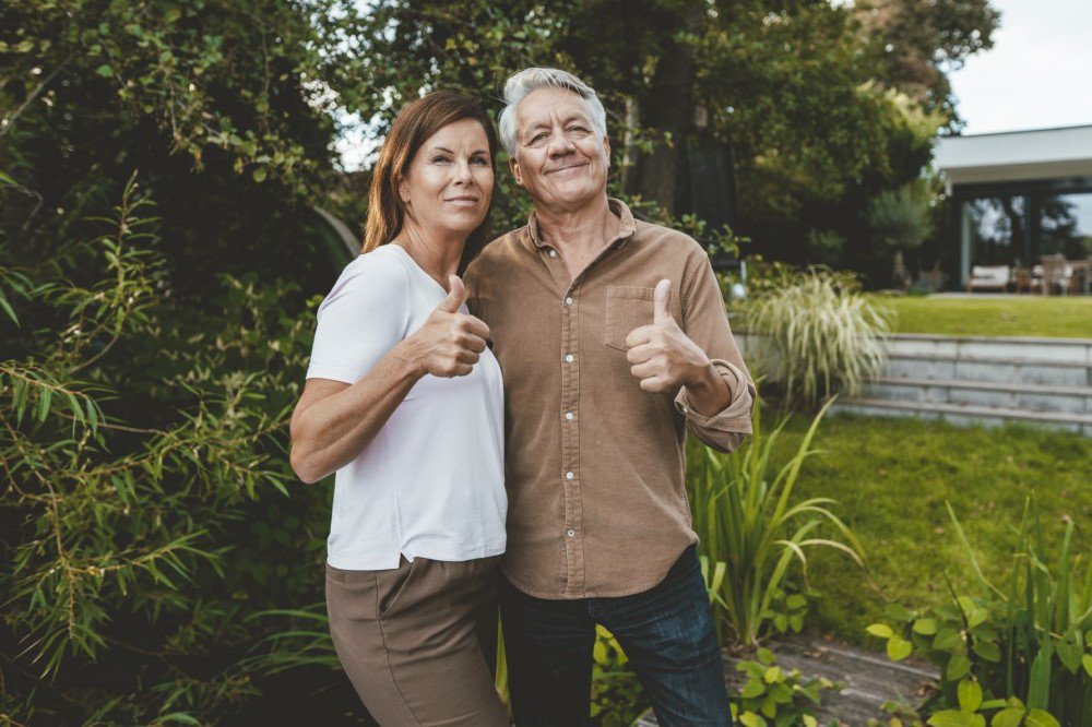 Mann und Frau stehen zufrieden im Garten mit Daumen hoch 