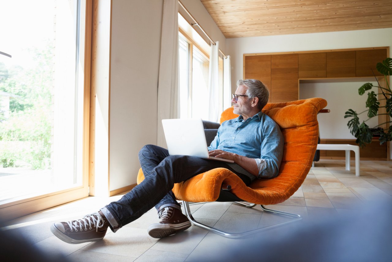 Mann mittleren Alters mit Brille sitzt entspannt auf Sessel mit Laptop