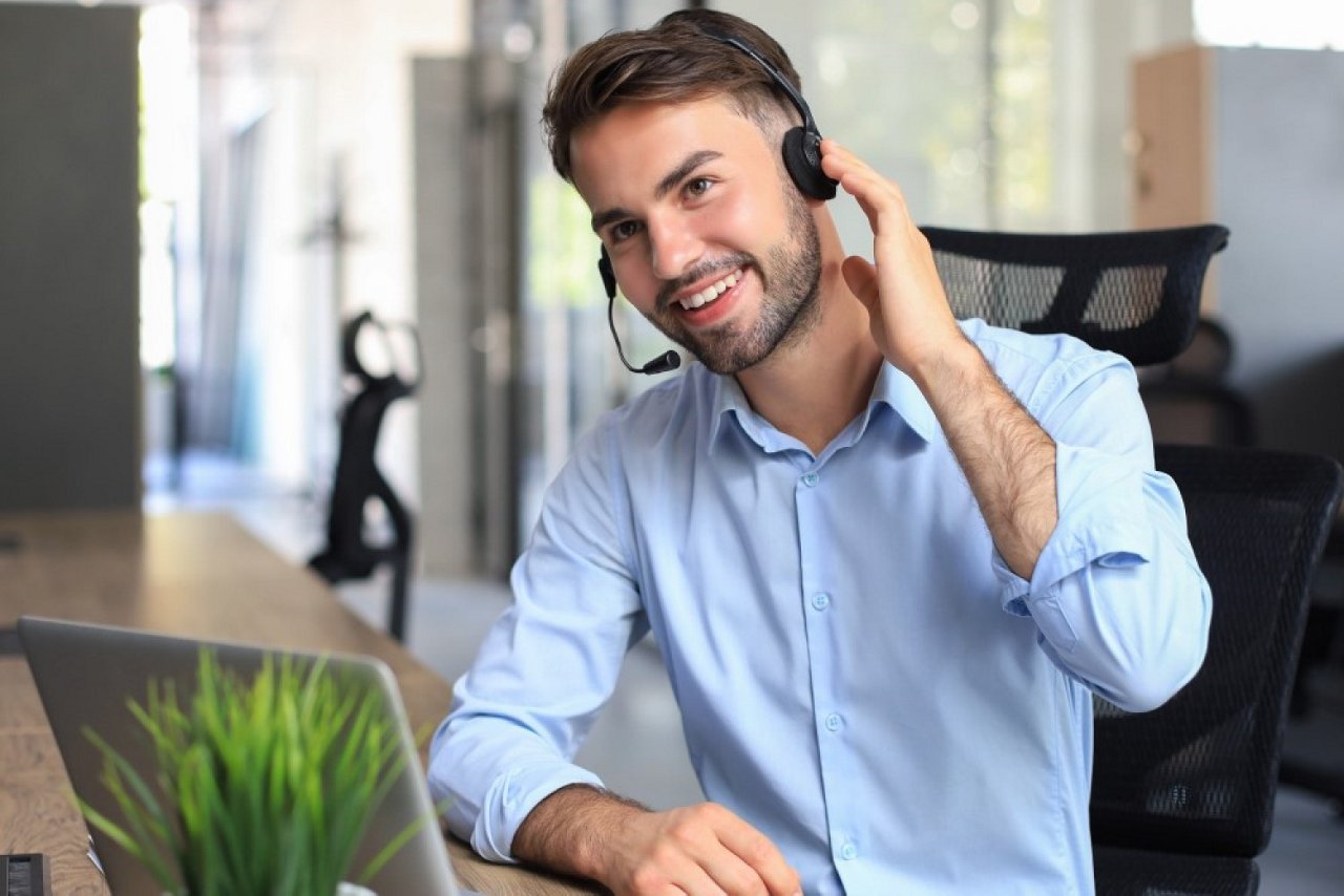 Mann in blauem Hemd sitzt vor Laptop und hat Headset auf