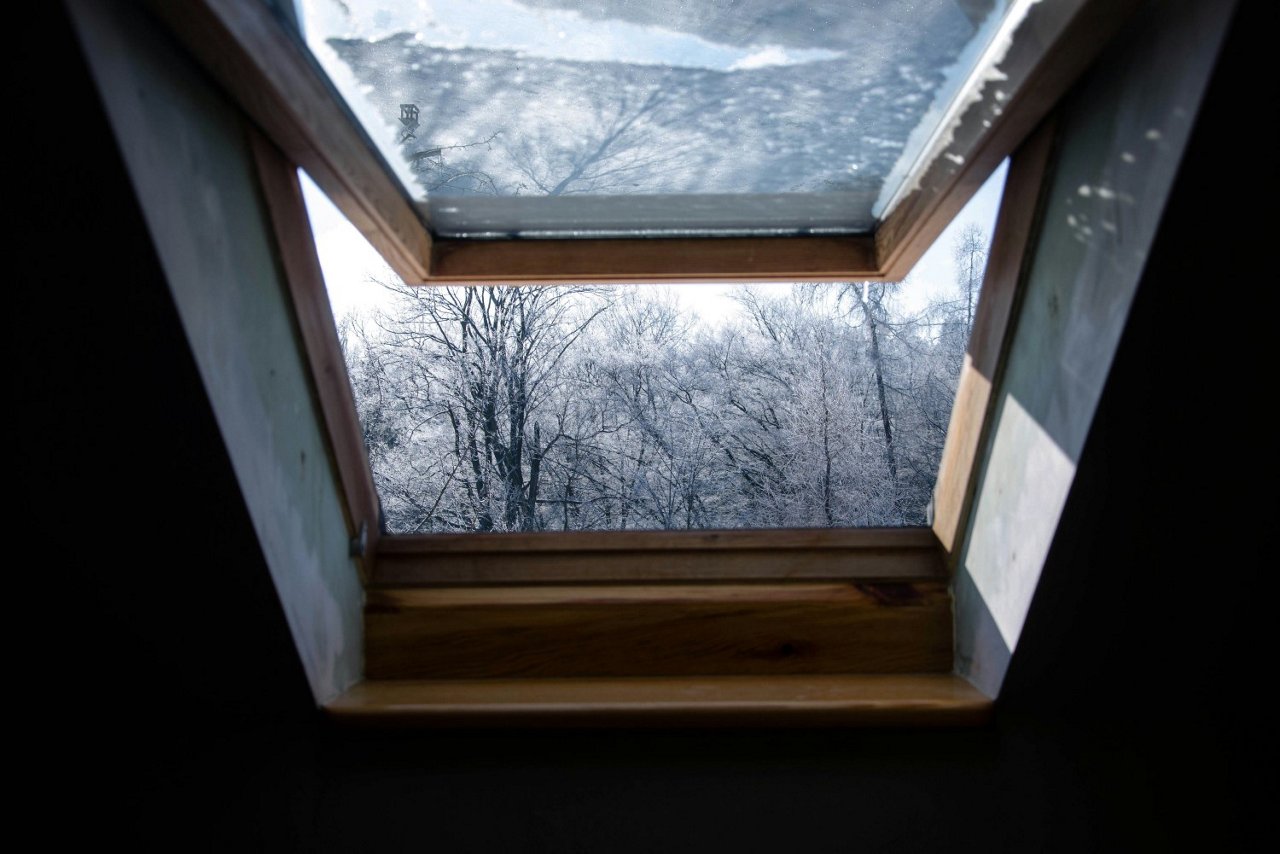 Geöffnetes Dachfenster mit Holzrahmen zeigt eine winterliche Landschaft mit frostbedeckten Bäumen