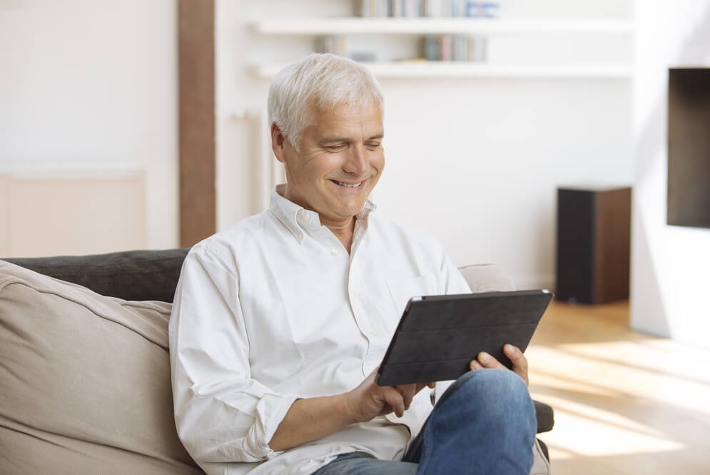 Älterer Mann sitzt auf der Couch vor einem Tablet