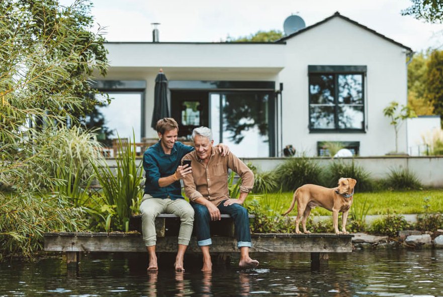 Vater und Sohn sitzen im Garten am Wasser und schauen in ein Smartphone