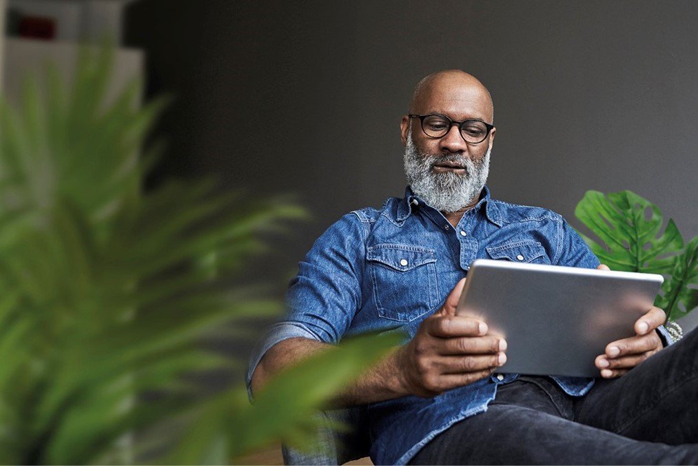 Älterer Mann mit Brille, der im Sitzen ein Tablet benutzt 