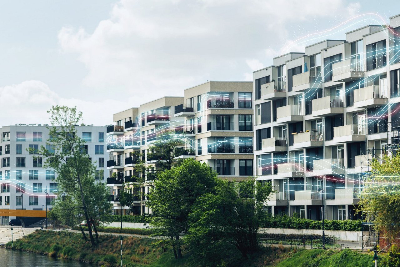 Moderne Wohngebäude mit Balkonen entlang eines Flussufers, umgeben von Bäumen und bewölktem Himmel